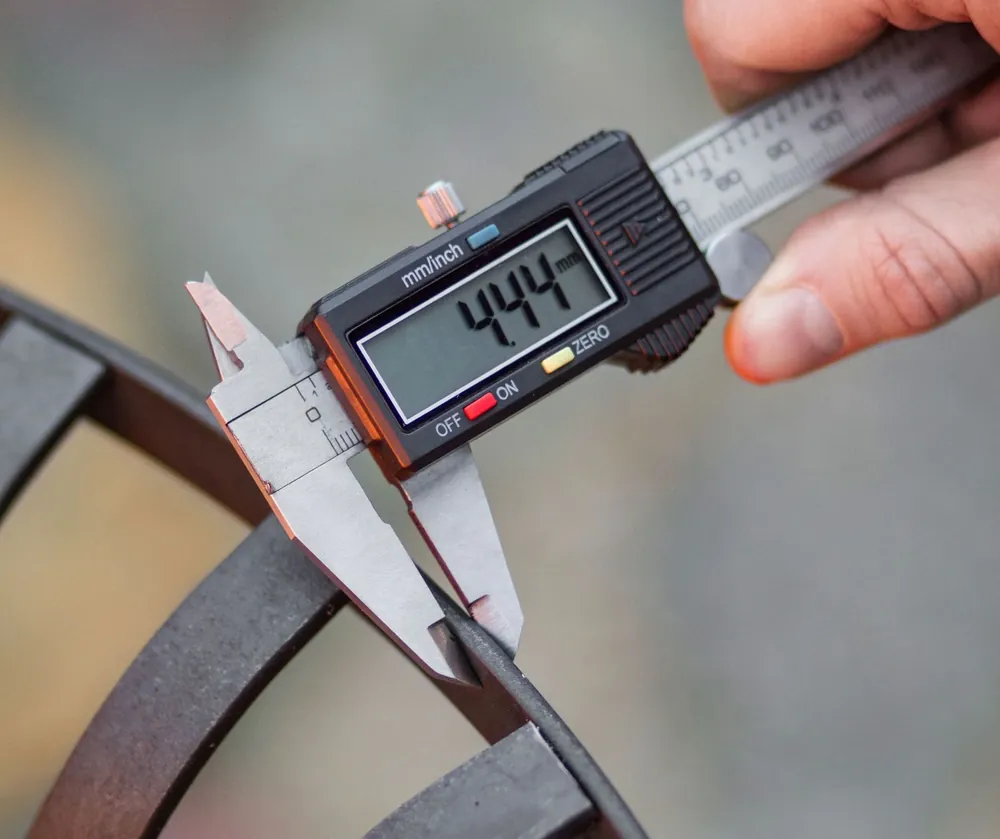Measuring the steel thickness of a COOK KING fire bowl with a caliper