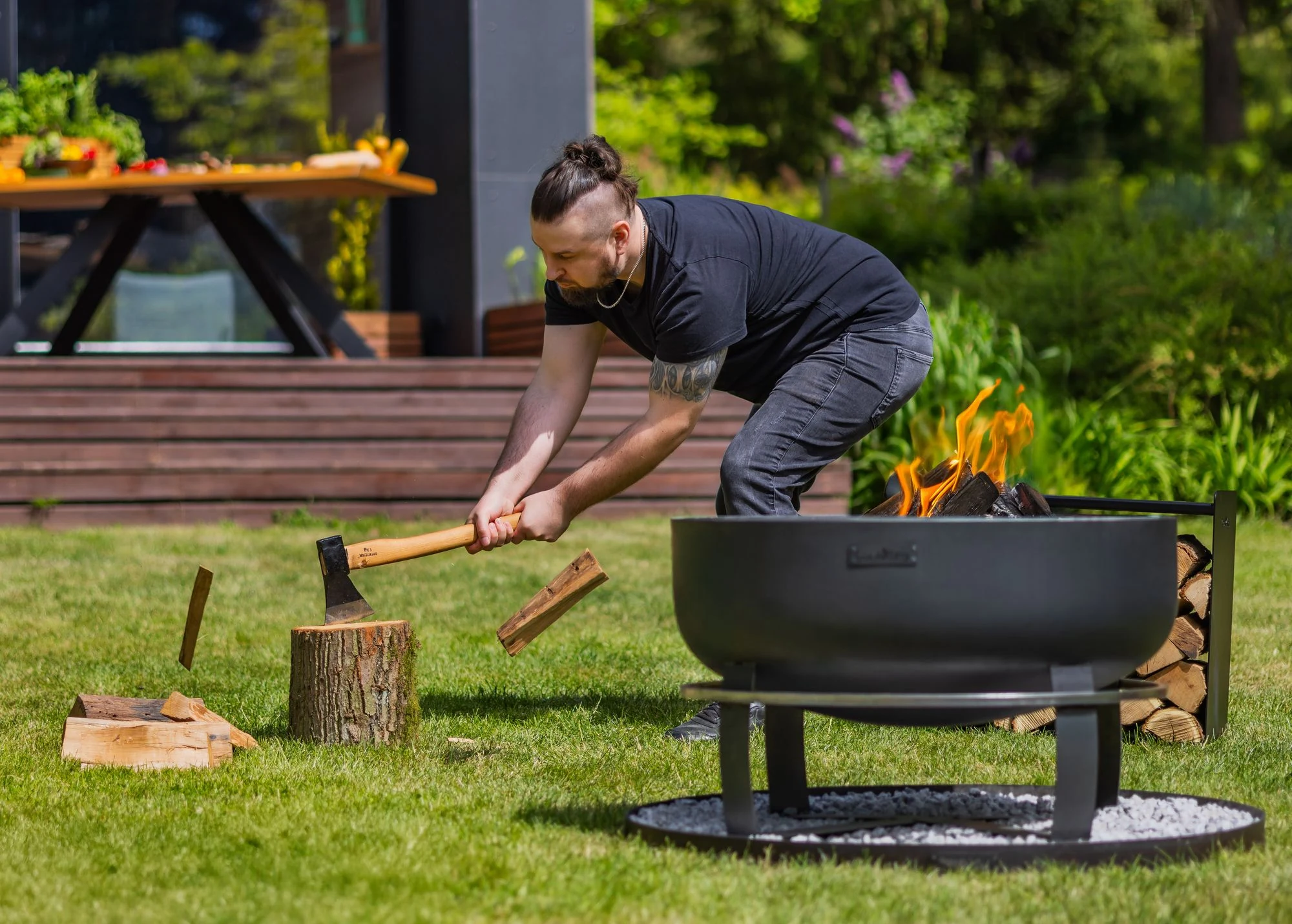 Man splitting firewood next to a COOK KING fire bowl