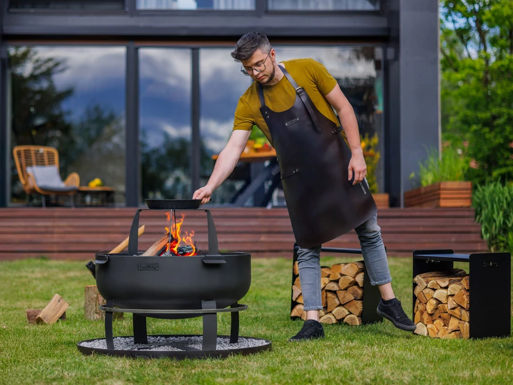 Man in an apron placing a grate in a COOK KING fire bowl